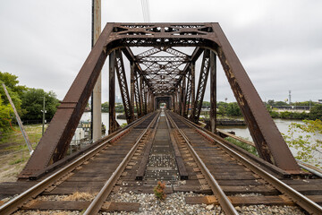 Fototapeta na wymiar Two railroad train tracks lead into a rusty metal trestle bridge crossing the Schuylkill River in Philadelphia, Pennsylvania, USA