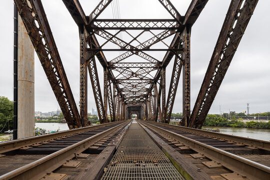Two railroad train tracks lead into a rusty metal trestle bridge crossing the Schuylkill River in Philadelphia, Pennsylvania, USA