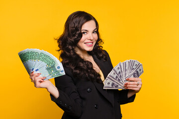 Rich woman in black jacket holding two cash fans of hundred euro and dollar banknotes of money,...