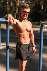 Cool athletic male bodybuilder with muscular naked torso training in the park