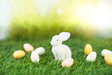 White Easter bunny figure on green lawn with easter eggs against bright sunny background