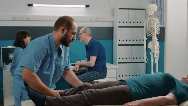 Physician and old patient doing legs raise exercise to help with recovery after physical injury. Male osteopath stretching muscles and using alternative medicine procedure to cure woman.