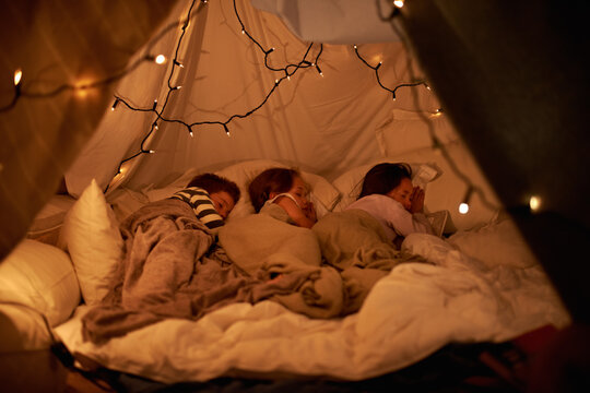 Sleeping in our imaginary tent. Shot of three young children sleeping in blanket tent.