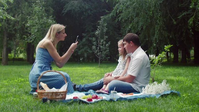 A woman takes photos of a child and a man at a summer picnic in nature on her phone