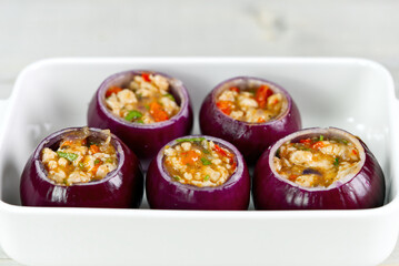 Stuffed onions recipe. Red onions stuffed with meat and vegetables in white bowl ready to bake in the oven. close up