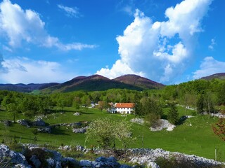 Obraz premium Rural landscape at the edge of Trnovo Forest Plateau in Littoral region of Slovenia with a meadow and a farmhouse in front and forest covered hills in the back