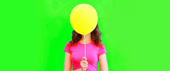 Portrait of funny woman covering her head with yellow balloon on green background