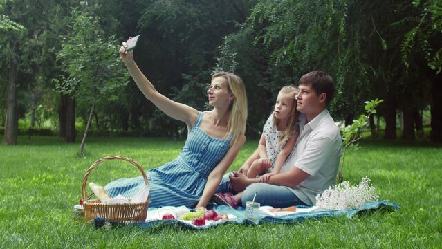 A woman takes pictures of herself, a child and a man at a summer picnic in nature
