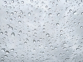 Raindrops on a transparent glass against a cloudy sky. Condensation and precipitation concept.