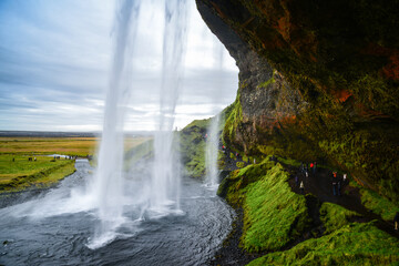 Tourists walking under Seljalandsfoss waterfall, southern Iceland