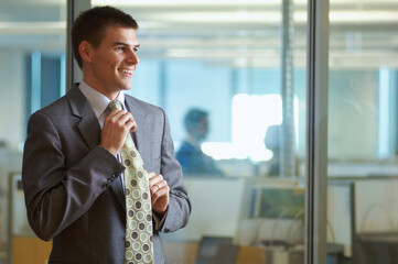 Smiling businessman in a business suit adjusting his necktie in the officee