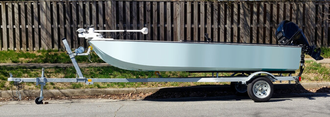 Side view of blue fishing boat on trailer parked on residential neighborhood street.