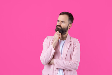 Handsome man with a beard in a pink jacket is thinking over an isolated red background.