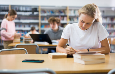 Fototapeta premium Teenage girl reading books and doing homework in library.