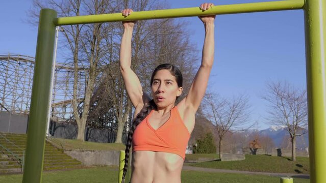 Athletic young woman doing pullups on bar at outdoor park