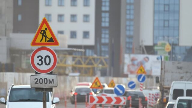 Roadworks warning traffic signs of construction work on city street and slowly moving cars