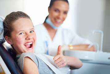 In the hot seat. Portrait of a young girl sitting in a dentists chair giving a thumbs up.