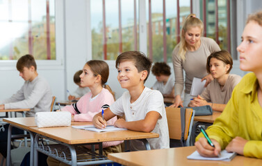 Fototapeta premium Teenagers sitting at desks in classroom during lesson and doing tasks.