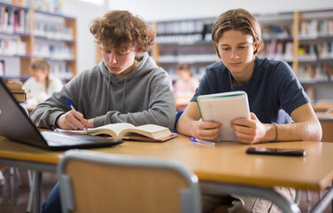 Teenage boys reading books and doing homework in library.