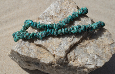 necklace of polished natural turquoise stones strung together and displayed on a chunk of rough quartzite