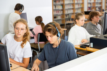 Teenager girls and boys studying in computer lab in library.
