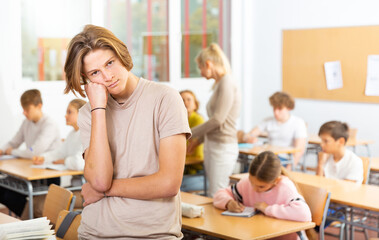 Stressed teenage boy feeling upset after getting bad mark at secondary school in class room - obrazy, fototapety, plakaty