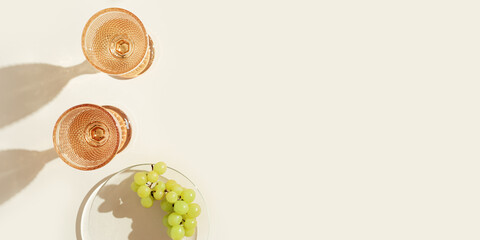 White wine glasses peach color glass and grapes fruit on beige background with dark shadow, glare...