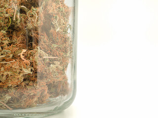 Dry cannabis buds flower in a jar glass over a white background