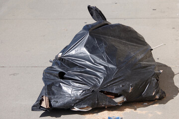 Black plastic bag with construction debris illegally dumped on a city sidewalk