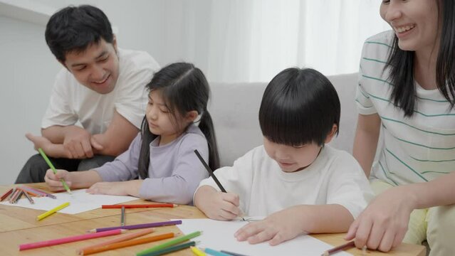 Asian family smiling laughing and having fun inside the house. Father and mother teach lovely son and daughter to draw and paint. Relaxing vacation and family happiness together. Holiday activities.