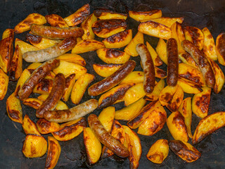 Barbecue sausages baked with potatoes on the baking tray and silicone mat
