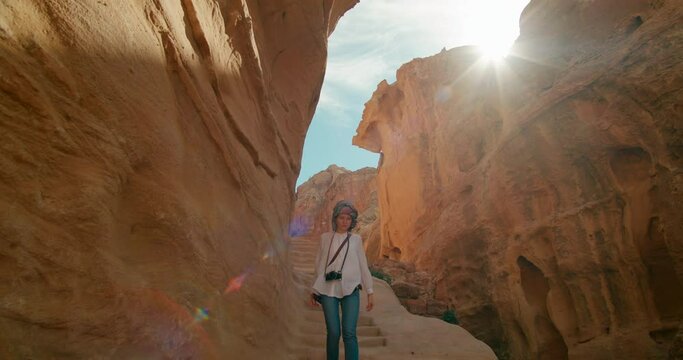 Tourist woman in turban visits Petra, Walking in Canyon in ancient Red Rose City. Traveling Girl hikes in rock gorge. Most popular attraction in Jordan, Middle East. 4K tracking gimbal medium shot