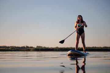 Low-angle of Caucasian woman standing on sup board with one oar in hands looking up at sky on...