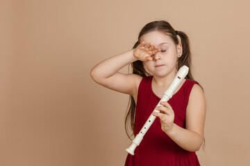 Girl in red dress hold flute with fingers and rub eyes from tiredness, beige background. Learning...