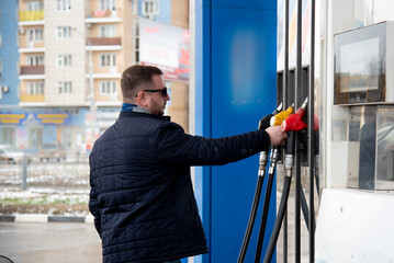 A man with a blue jacket and dark glasses at a gas station. He fills up the car. Petrol. Lifestile.