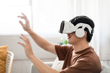 Technology Concept The man with his brown T-shirt and light blue jeans wearing a virtual reality headset while sitting on the sofa