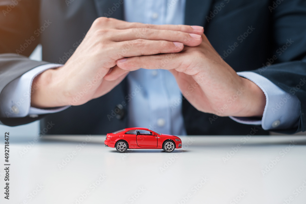 Wall mural Businessman hand cover or protection red car toy on table. Car insurance, warranty, repair, Financial, banking and money concept