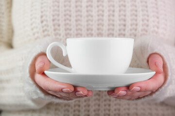 White cup in female hands. Tea in a white cup in a female hand on the background of a knitted sweater. Elegant female hands holding a white cup for coffee.