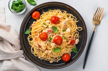 Fetapasta, spaghetti with baked feta, cherry tomatoes, herbs and basil on a gray background.