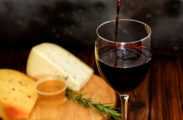 Red wine being poured into glass with cheese board in the background