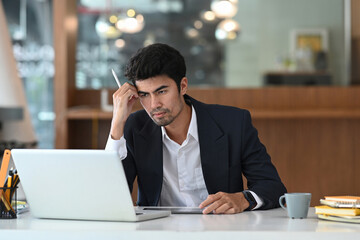 Obraz premium Serious businessman looking at his laptop while sitting at his workplace.