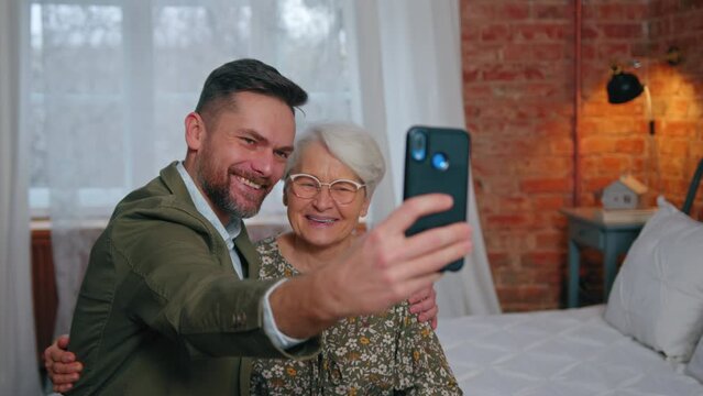 happy grinning elderly mother and her middle-aged millennial son taking a silly photo of the two of them. High quality 4k footage