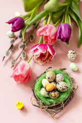 Obraz na płótnie Canvas Pink and purple tulips with colorful quail eggs in a nest over pink background. Spring and Easter holiday concept.
