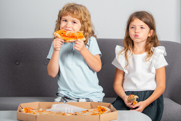 Children eating pizza. Two young children bite pizza indoors.