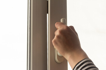A hand opens a window in an apartment or house for ventilation.