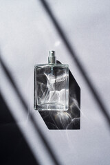 Transparent bottle of perfume with spray on a grey background. Beautiful natural light and shadows....