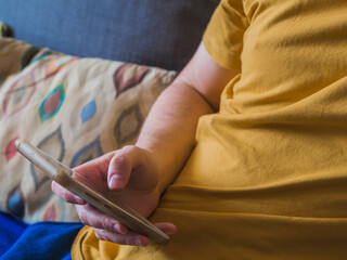 Hand of caucasian man with yellow t-shirt looking the social media from the smartphone