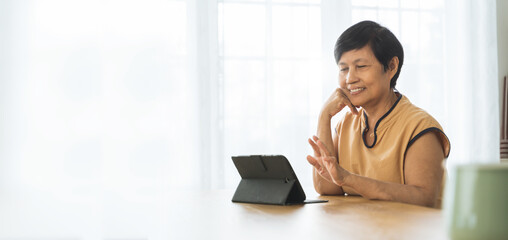 Asian Mature woman using digital tablet computer at home, Online Video call with family.