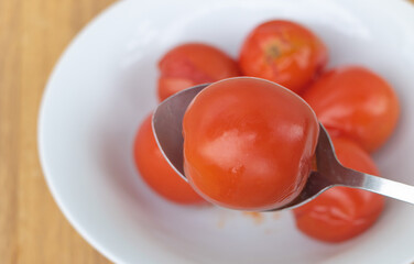 Close up shot of marinated tomatoes in a white plate with wooden background - A spoon with tomatoes