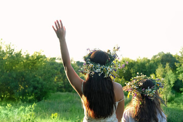 Two girls in flower wreaths on meadow, sunny green natural background. Floral crown, symbol of...